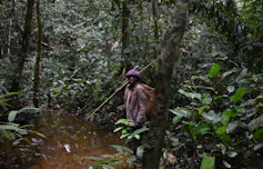 Un homme se tient dans une forêt tropicale dense, tenant de longs bâtons