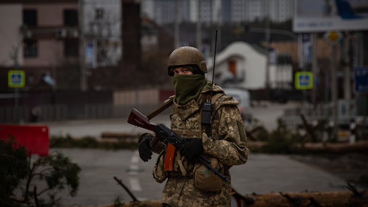 A Ukrainian soldier standing guard in a war-damaged town.