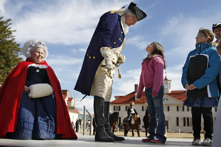Two people in costumes talk to school children outdoors.