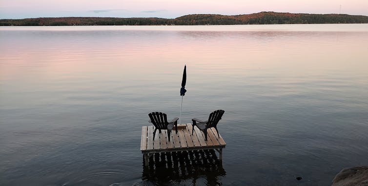 Flota con dos sillas y un paraguas en el lago al anochecer hasta que el agua brille el rosa.