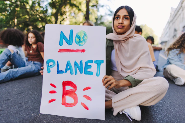 A young woman sits holding a sign saying 'no planet B'.