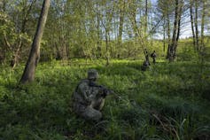 An armed soldier in a dense green forest.