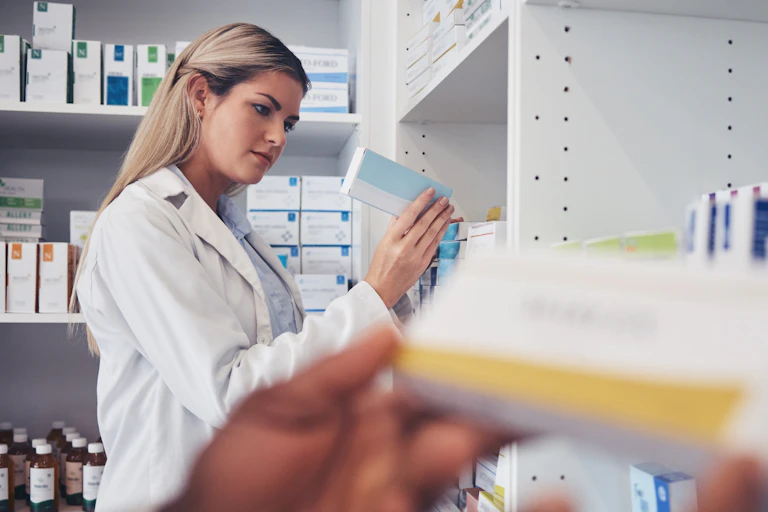 une femme dans une pharmacie avec une boite de ce qui semble être un médicament à la main