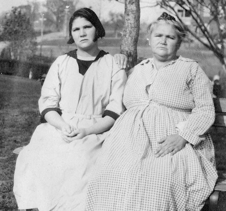 Two women sit next to each other and look at the camera in a black-and-white photo.