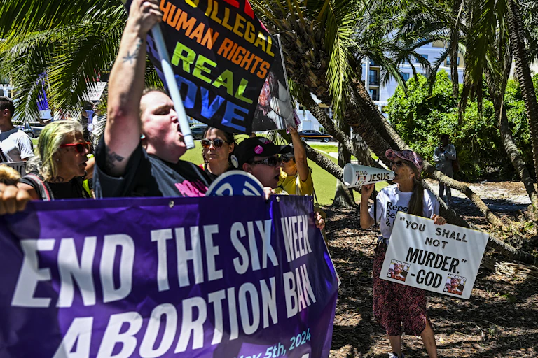 Protesters carry a large banner reading 'End the Six-Week Abortion Ban' as they march.