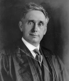 A black-and-white photograph of a white man wearing a tie and judge's robes.