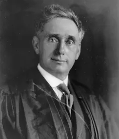 A black-and-white photograph of a white man wearing a tie and judge's robes.