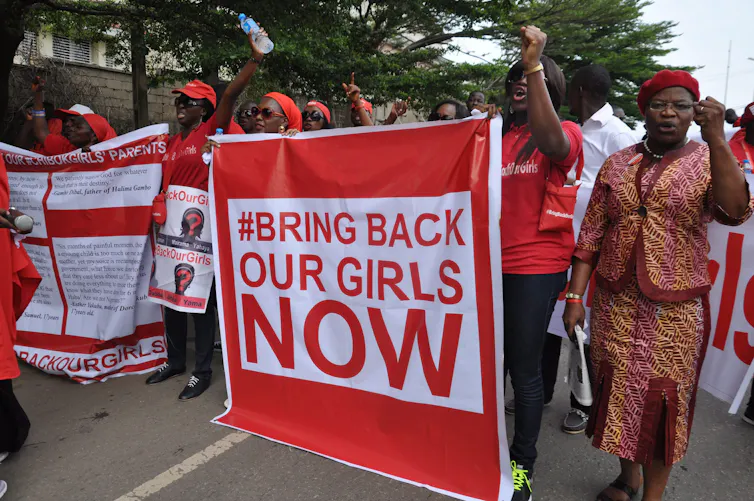People march at a demonstration carrying a large red sign reading: bring back our girls now