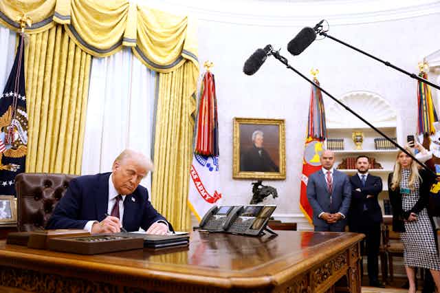 a man in a business suit signs a document in an ornate office
