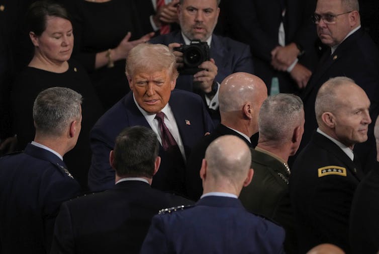 A man in suit and tie in a crowd of people, including men in uniforms.
