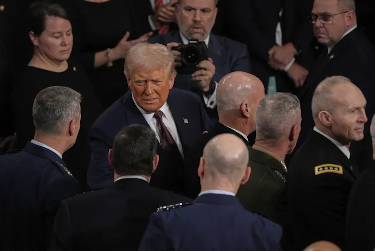 A man in suit and tie in a crowd of people, including men in uniforms.