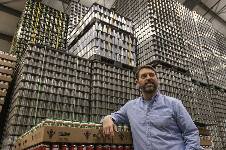 A man stands in front of stacks of aluminum beer cans in a warehouse