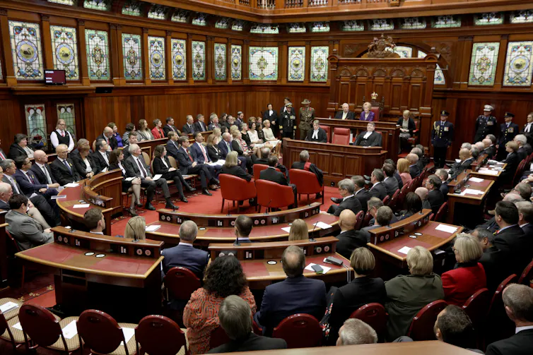 A wooden parliamentary chamber with people sitting on sitting in a horseshoe shape