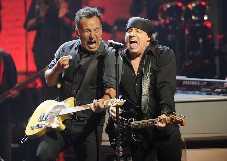 Two men perform on a stage with guitars.