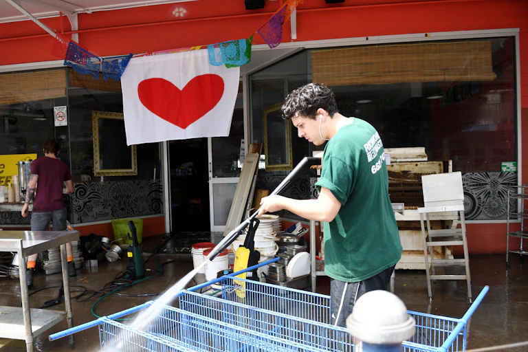 man hoses pavement after floods with heart sign in background