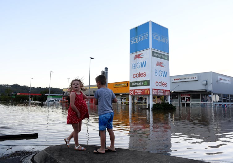 Two children stand before flooded streets and shops