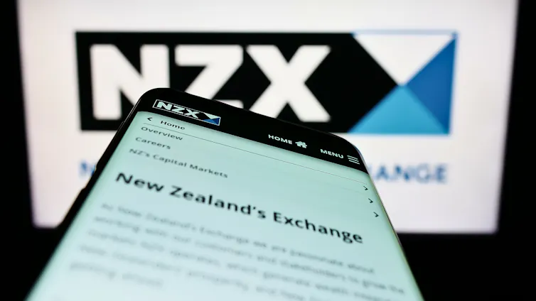 Photo of NZX photo with mobile listing of the NZX website in front of it.