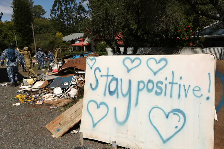A sign saying 'stay positive' in front of flood debris