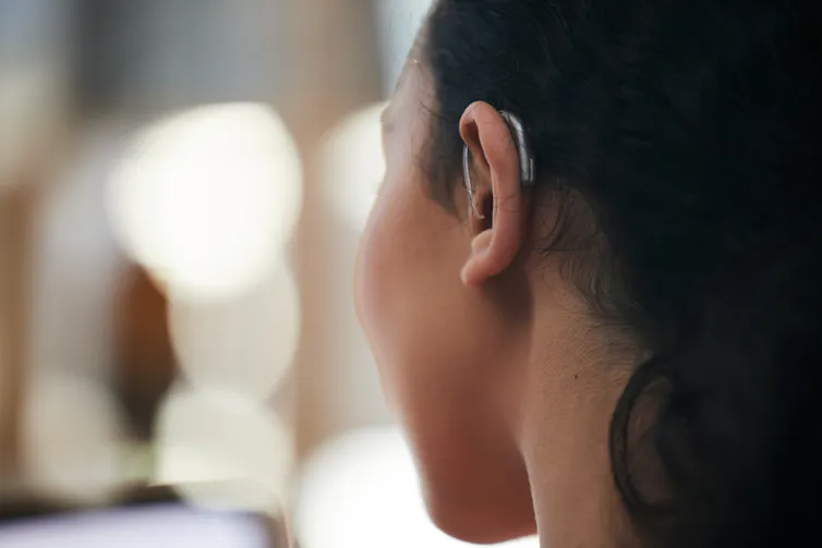 A younger woman sports a small hearing aid on the back of her ear.
