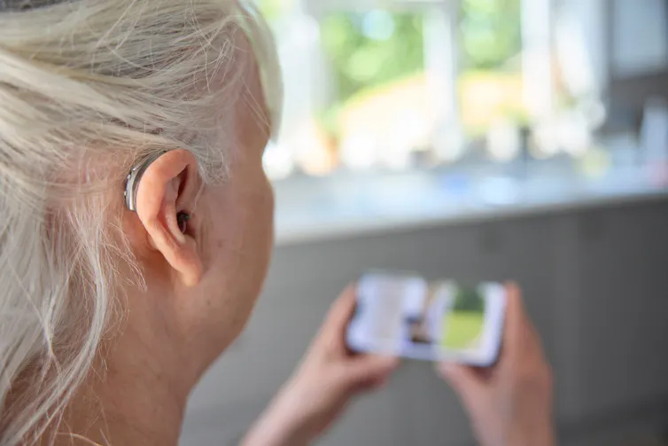 A woman in a hearing aid watches a show on her phone.