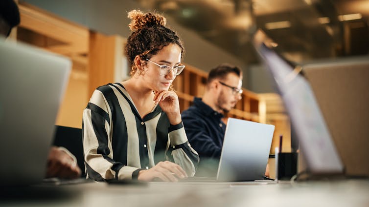 Young colleagues sitting side by side at a desk, working on laptops