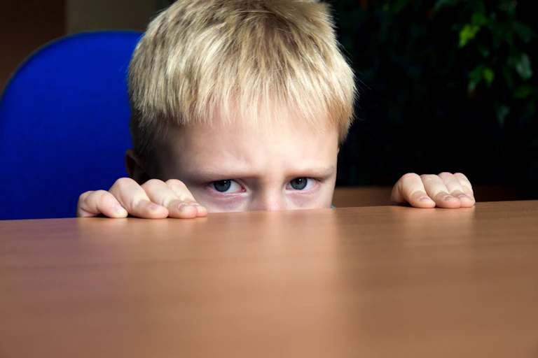Un enfant qui se cache derrière une table.