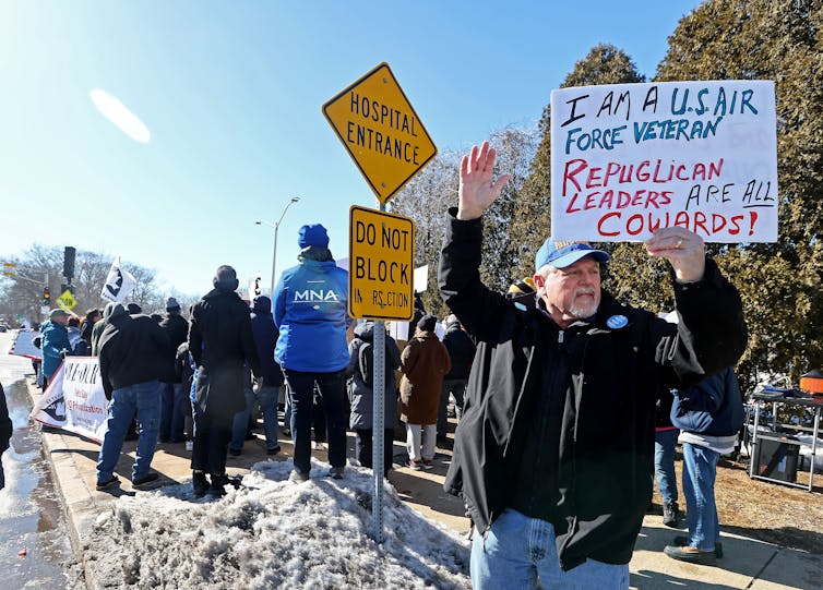A man standing with a sign that says 'I'm a USAIR Force veteran Republican leaders are all cowards!'