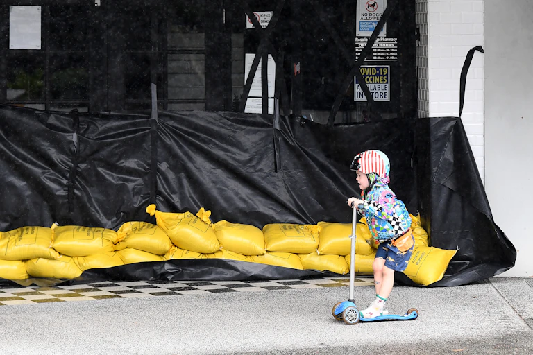 A young child scoots past a sandbagged shop.
