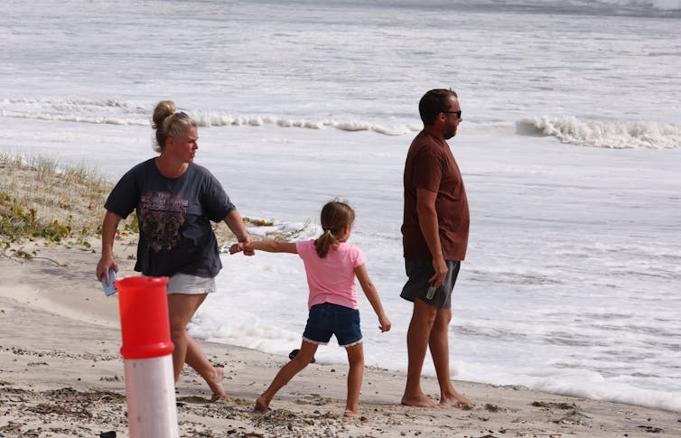 A woman, man and young child look at the swell at a beach.