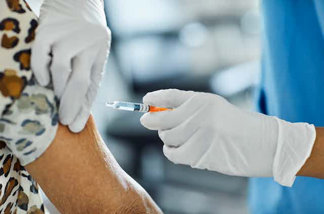 Cropped image of health care worker in white gloves administering a COVID vaccine into the arm of an older adult