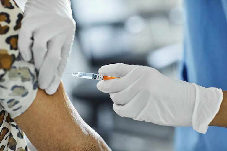 Cropped image of health care worker in white gloves administering a COVID vaccine into the arm of an older adult