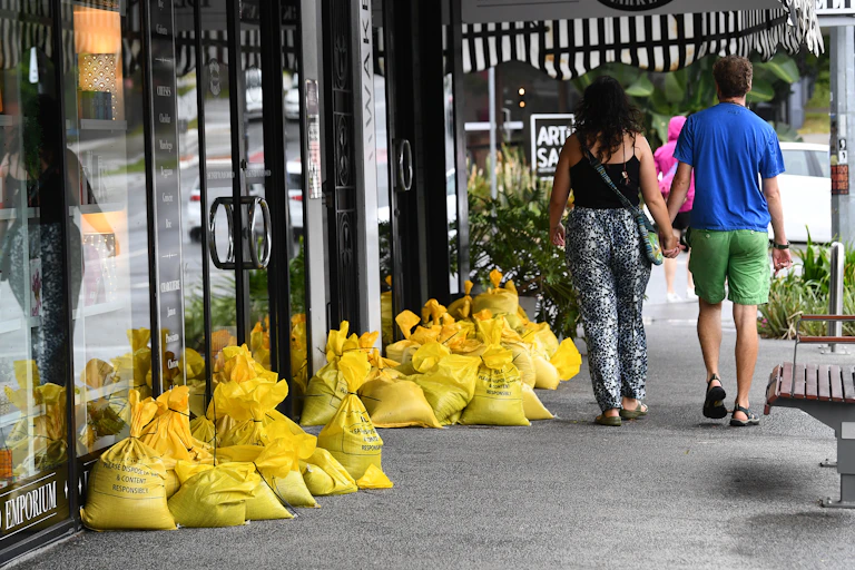 couple holding hands walks past sandbags and shops