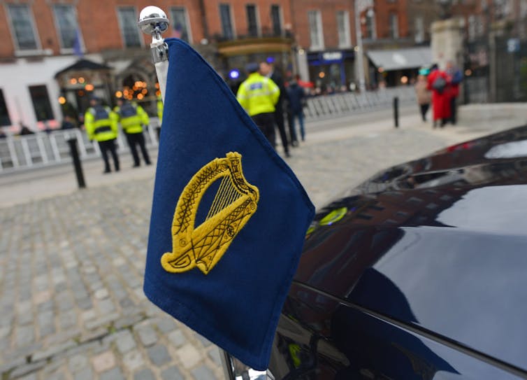 A small, dark blue flag with a gold harp on it is affixed to the hood of a black car.