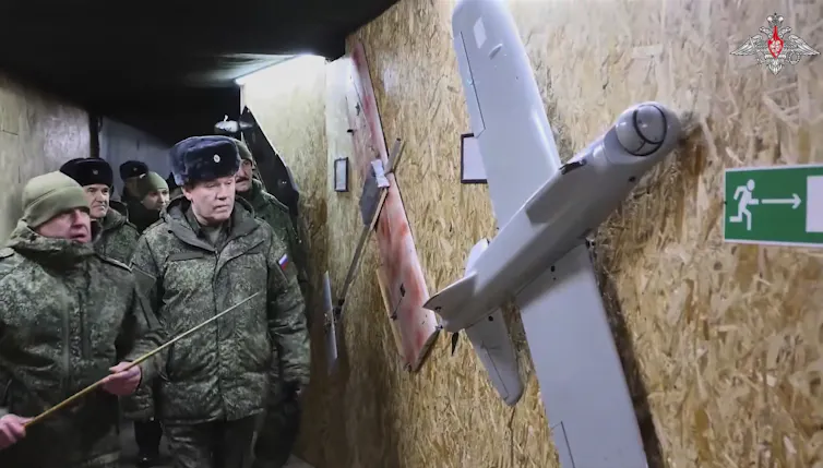 Men in military fatigues look at a small drone hanging on a wall
