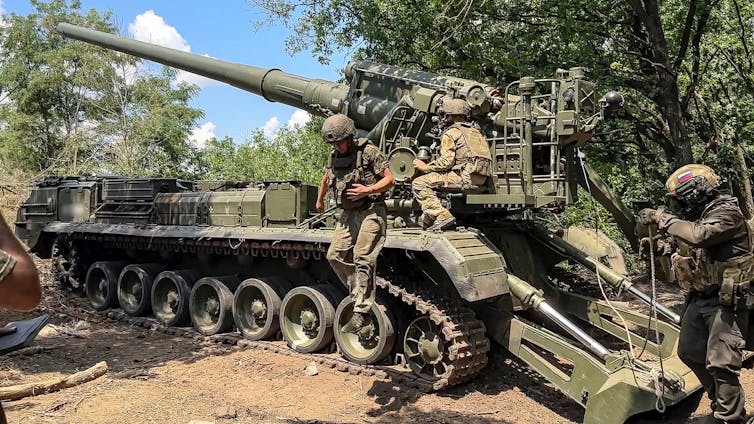 Men in military fatigues near a tank with a large cannon pointed at an upward angle