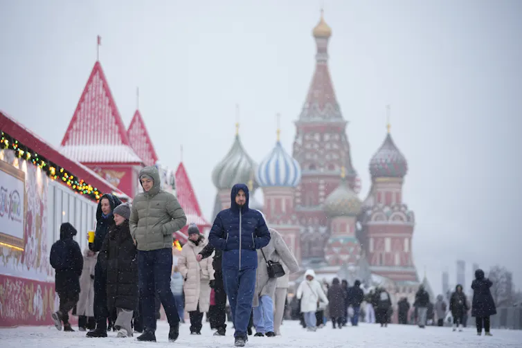 People walk during snowfall. The colourful towers of St. Basil's Cathedral are in the background.