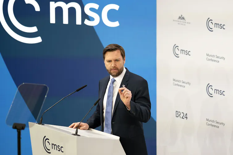 A man with dark hair and a beard speaks from behind a podium.