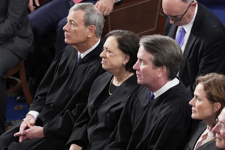 Two men and two women sit in a row at a gathering.