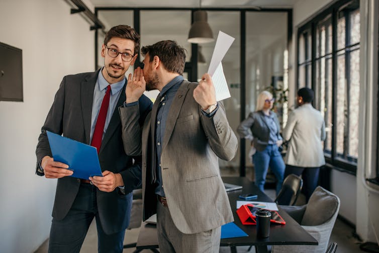 Two coworkers gossiping and having a discussion in a modern office.