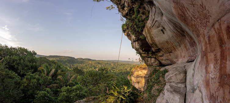 rock art on overhanging cliff, landscape with trees to the left