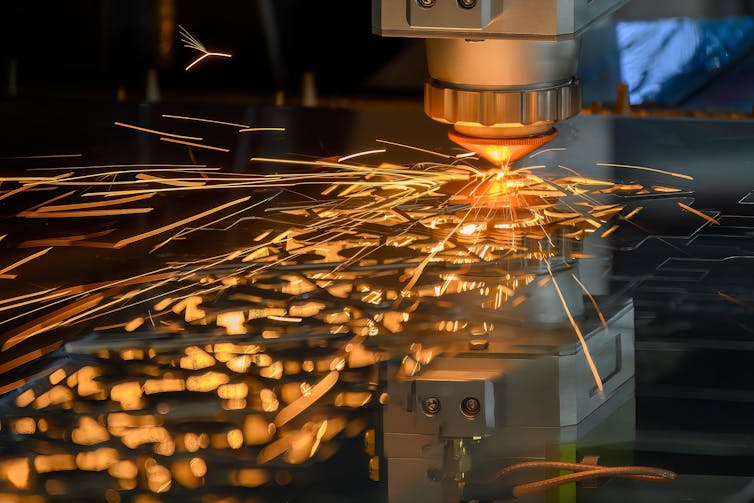 Close-up of a fiber laser cutting machine cutting a metal sheet, with sparkling light flying off.