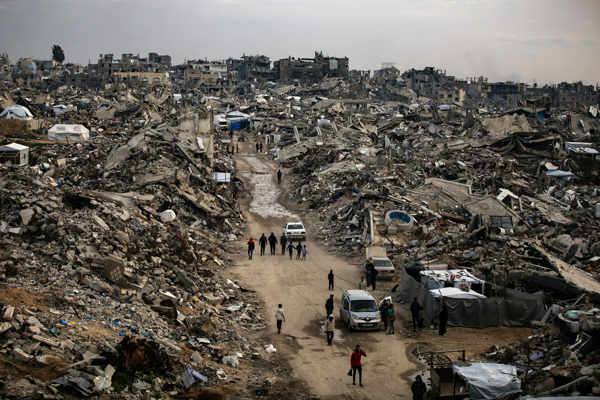 Palestinians walk among the rubble of a destroyed city.