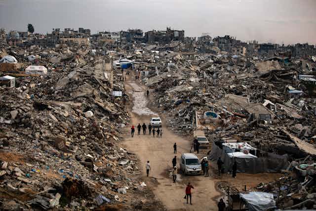 Palestinians walk among the rubble of a destroyed city.