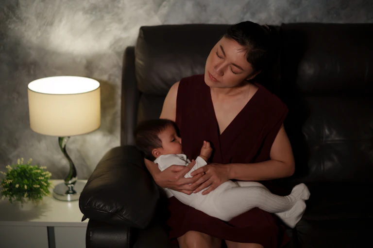 Une mère, assise sur un canapé, allaite son enfant.