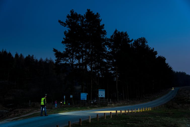 A country road at night, with two volunteers with head lamps and high-vis vests.