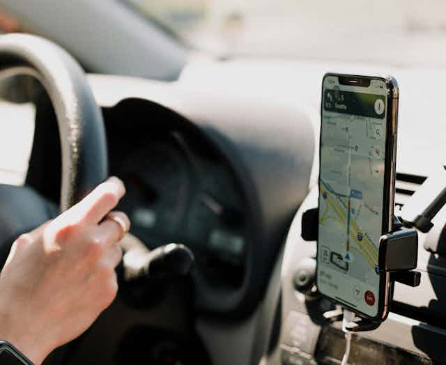Someone drives a car with their phone on display showing Google Maps.