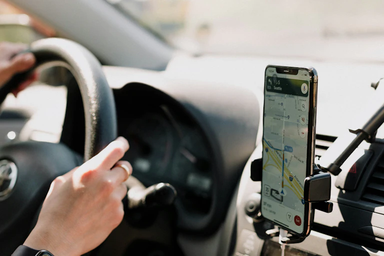 Someone drives a car with their phone on display showing Google Maps.