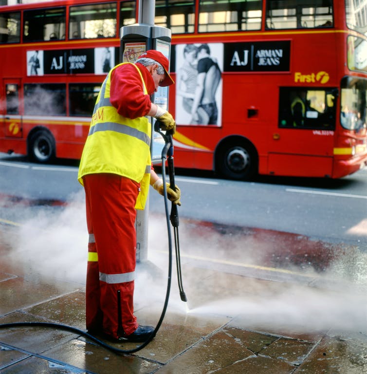 street cleaner steam cleaning urban street, red london bus in background