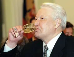 A man with white hair sips on a glass of champagne.