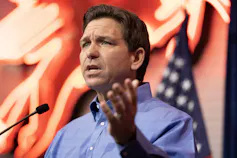 A middle-aged white man with brown hair speaks from behind a lectern